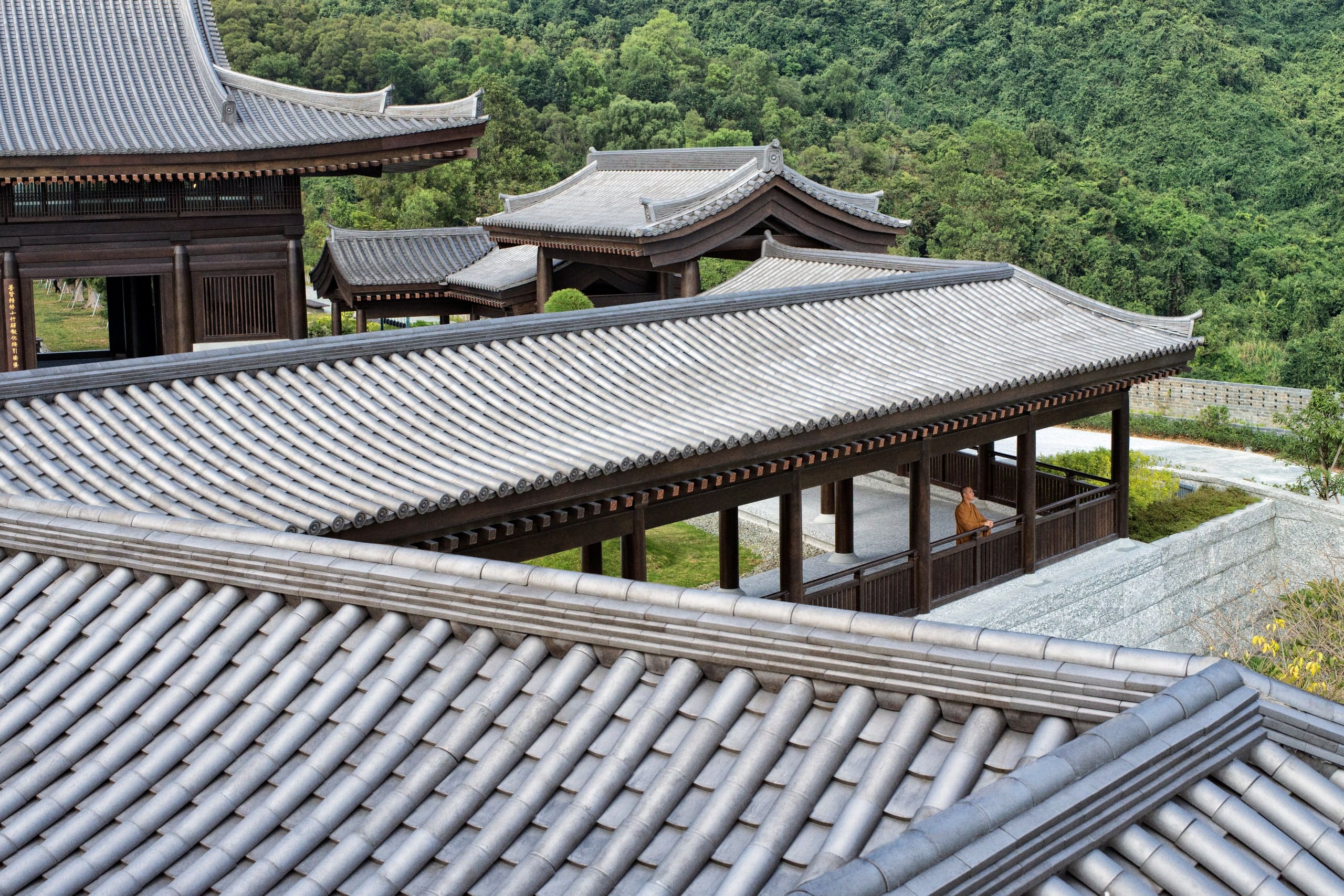 Tiled walkway roofs crossing above a courtyard, hillside behind.