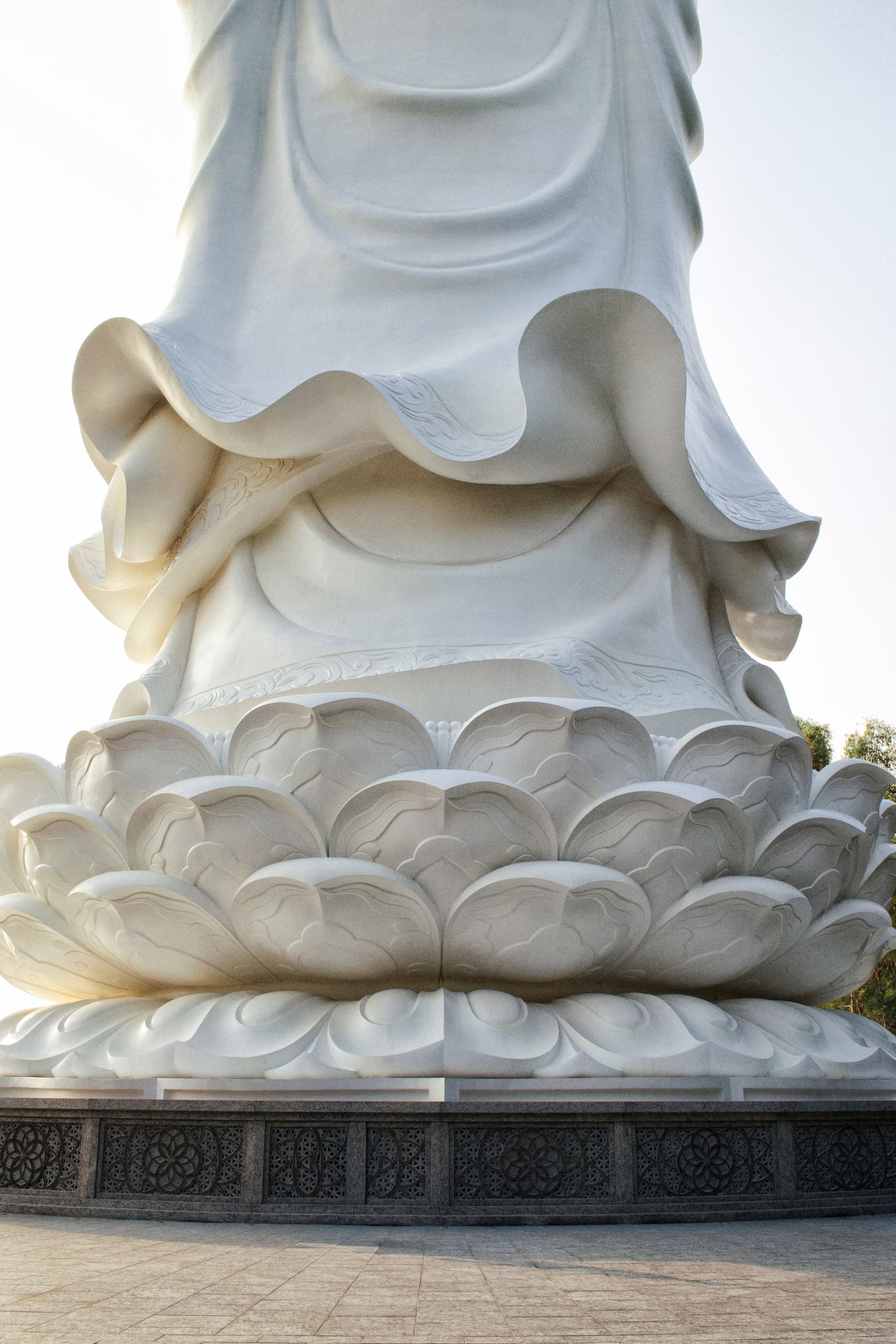 The statue's carved lotus base against a pale sky.