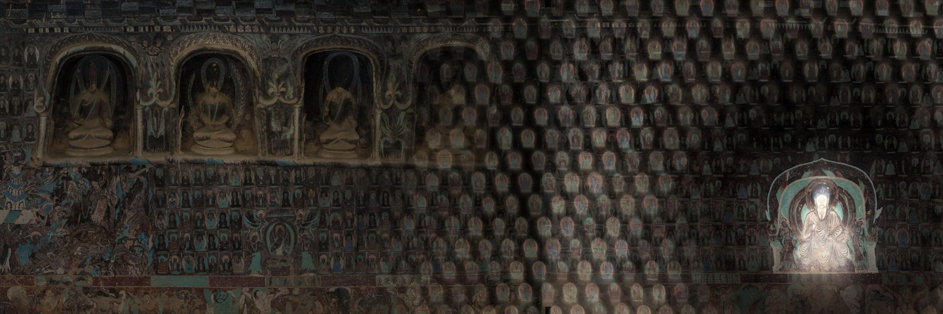 A painted cave wall of seated Buddhas, one figure lit in its niche.
